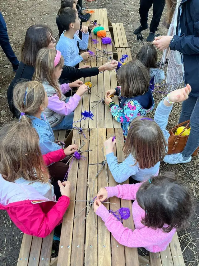 Gruppo di bambini seduti ai tavoli da picnic mentre intrecciano ragnatele con la lana