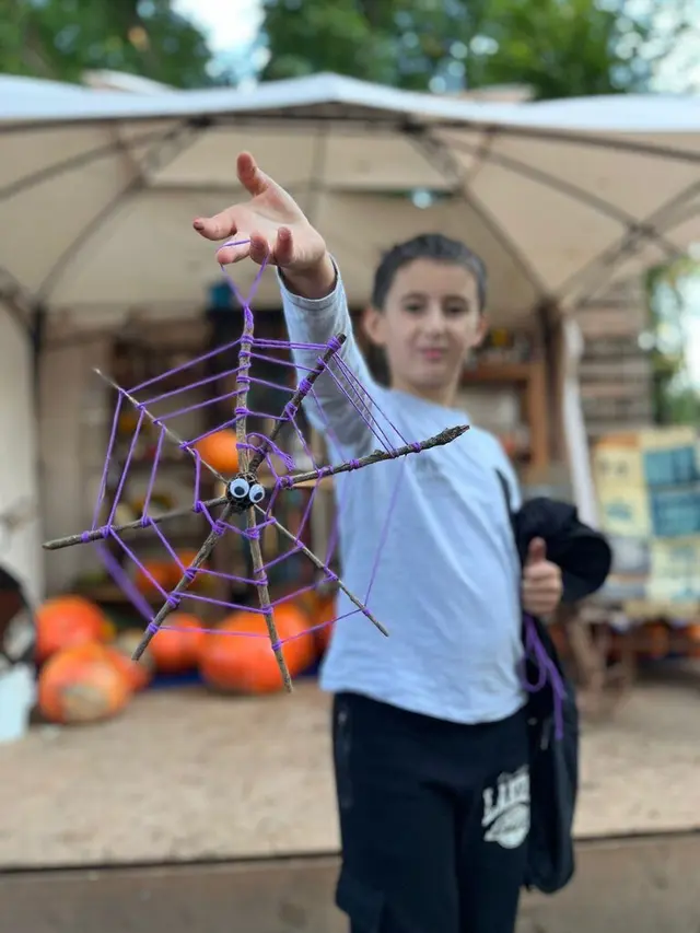Bambino mostra la ragnatela costruita con rametti e lana viola con un ragnetto al centro