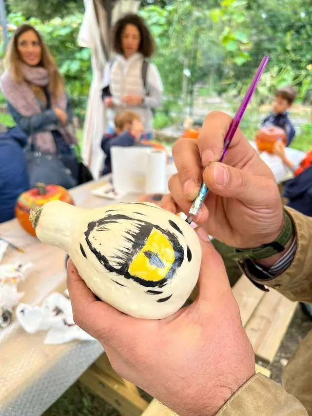 Mani di un adulto che dipingono un occhio nero e giallo su una zucca bianca